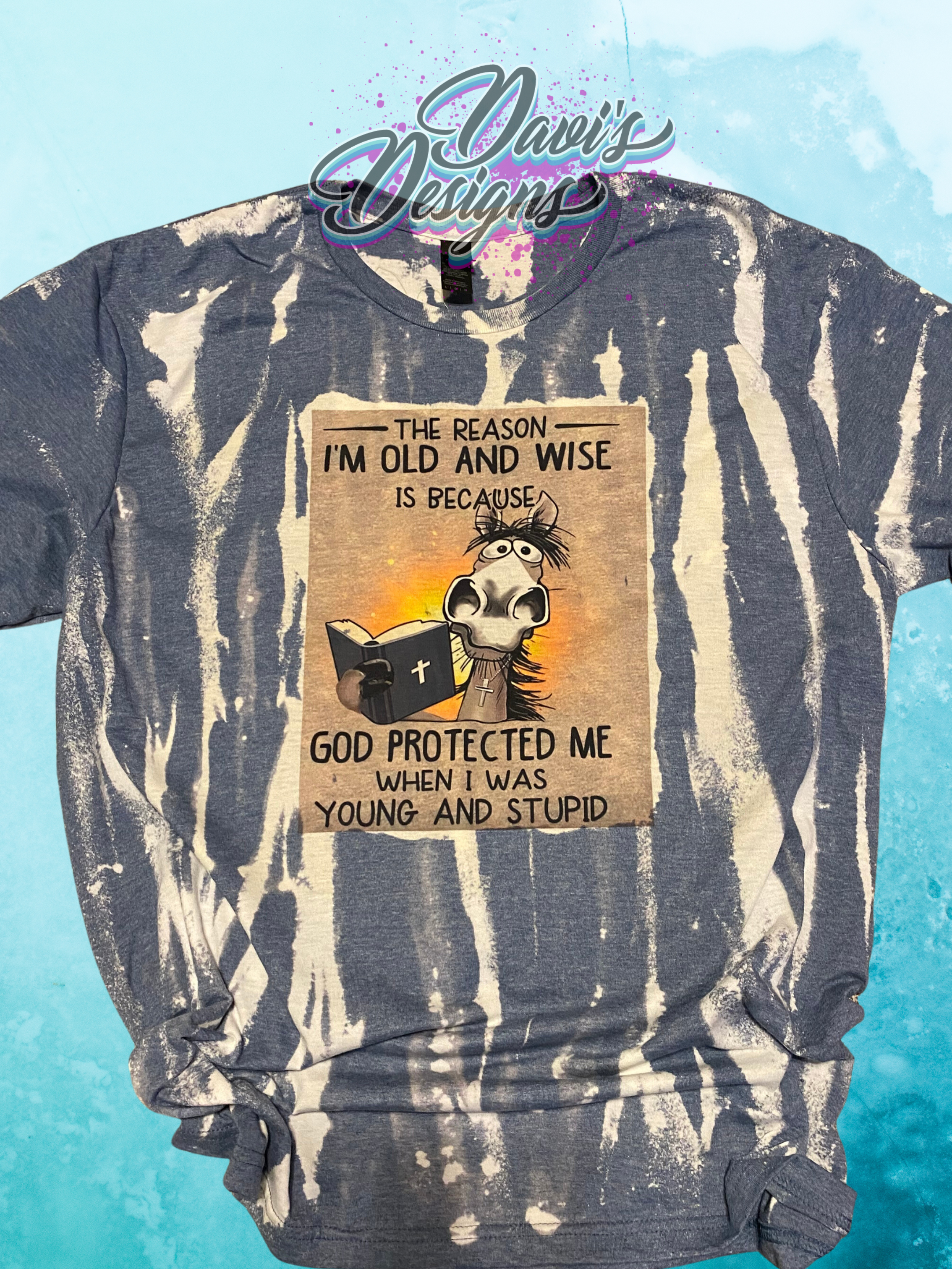 Heather Indigo bleach patterned tee with a horse holding a bible saying The Reason I'm Old and Wise is Because God Protected Me When I Was Young and Stupid.